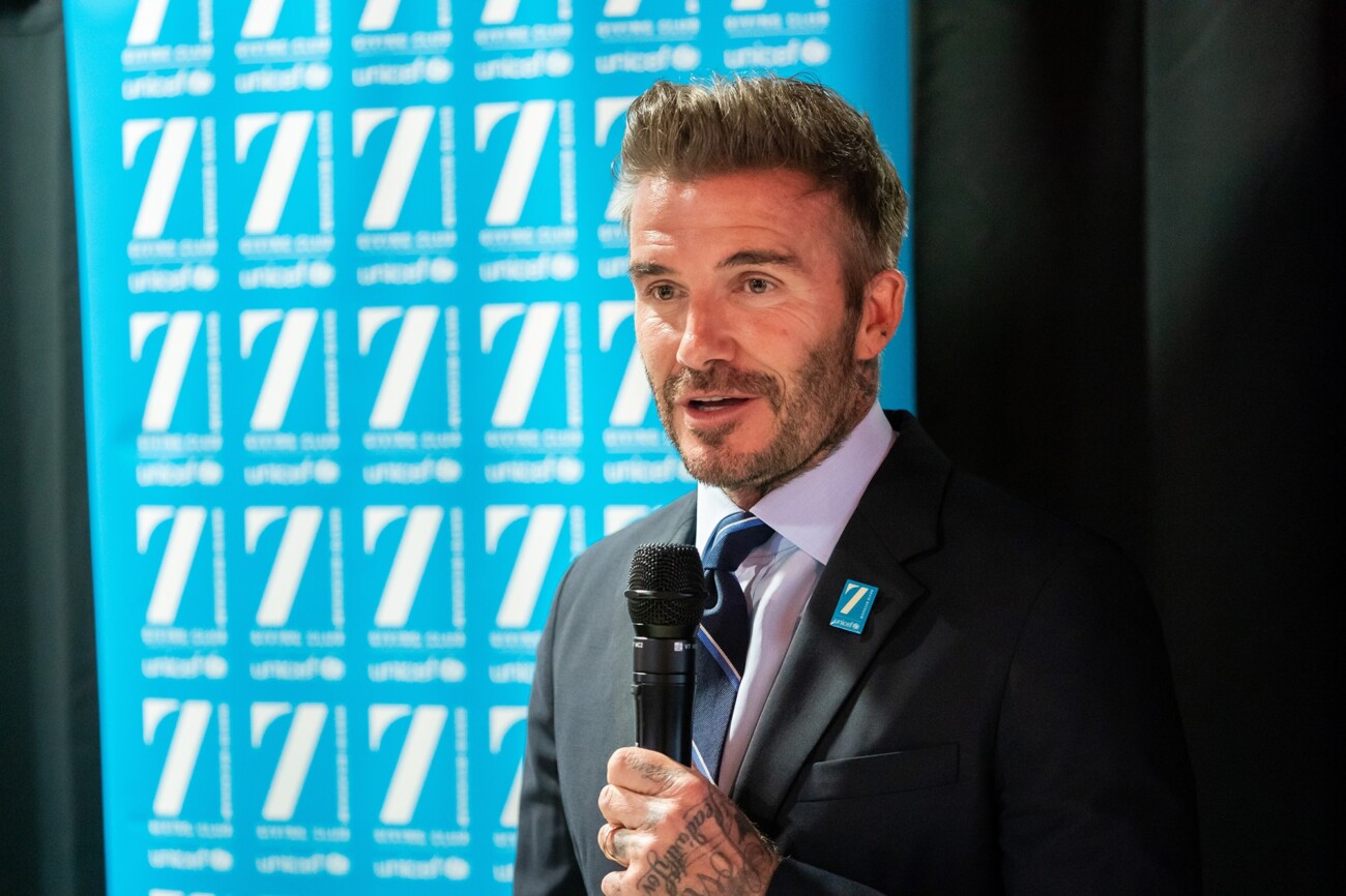 A man in a suit and tie is speaking into a microphone against a backdrop with repeating UNICEF logos