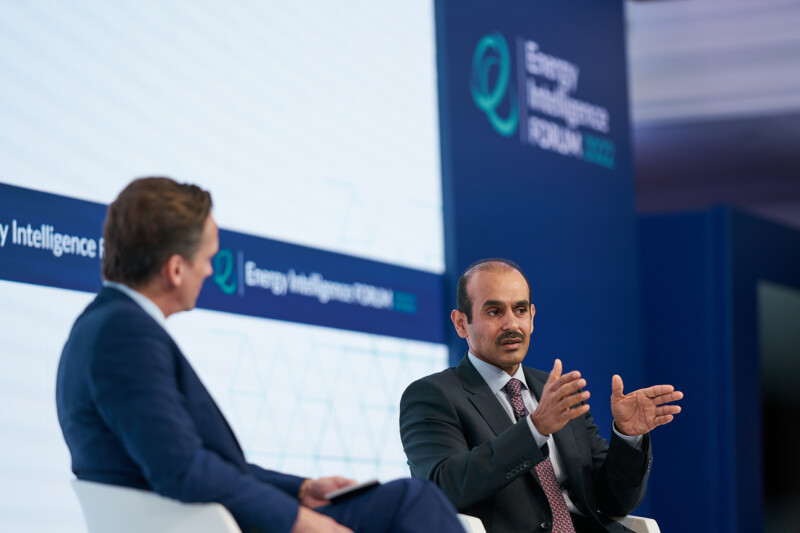 Two men are seated on a stage, deeply engaged in discussion at the Energy Intelligence Forum 2022 captured by a skilled London conference photographer. One man gestures animatedly as a large screen in the background proudly displays the event's logo and name. James Gifford-Mead Photography - Event Photographer London