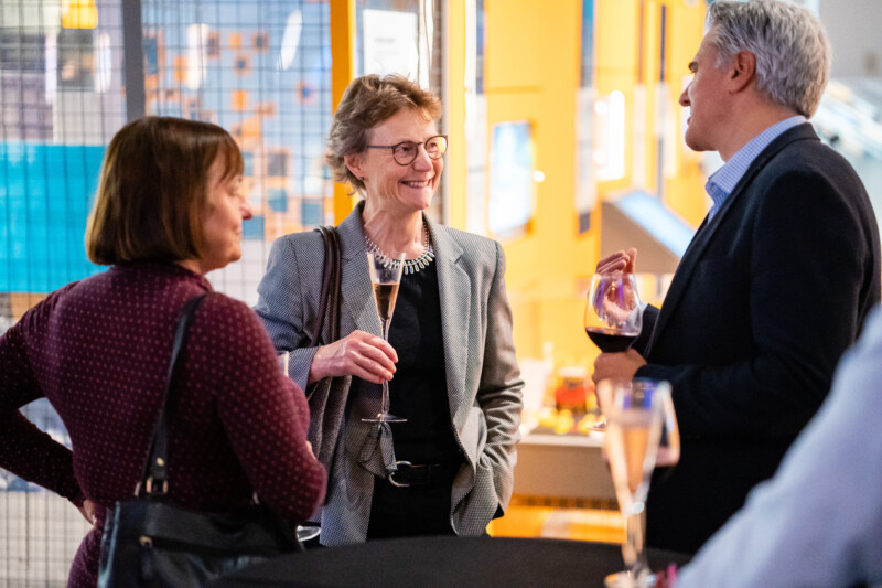 At a lively social gathering, three people converse with wine glasses in hand, framed by bright and colorful decor. Capturing this vibrant moment is akin to a London conference photographer's keen eye for atmospheric and engaging scenes. James Gifford-Mead Photography - Event Photographer London