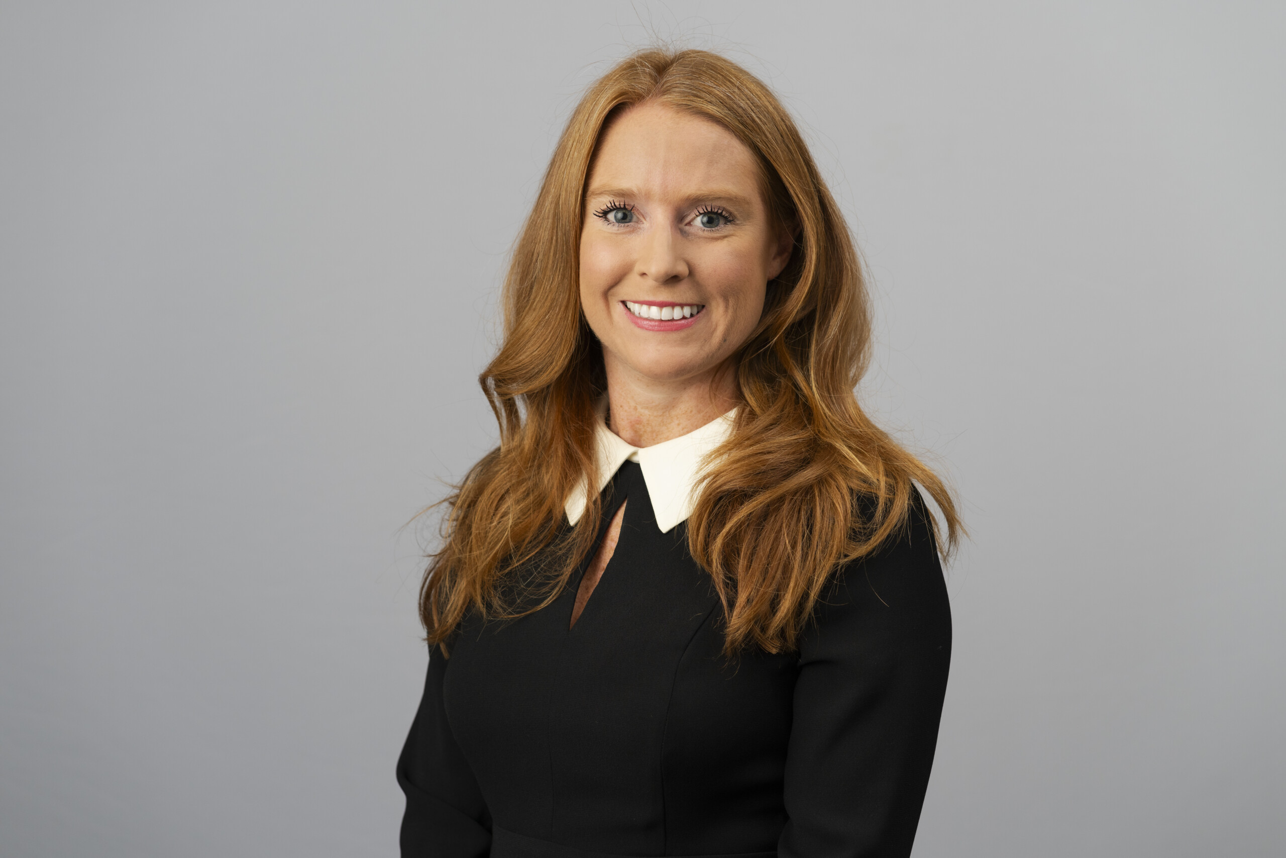 Professional corporate headshot against a grey background