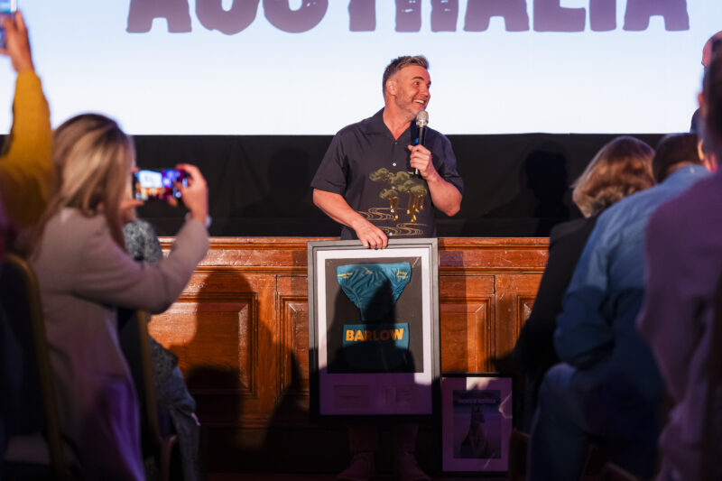 Man speaking on stage holding framed item.