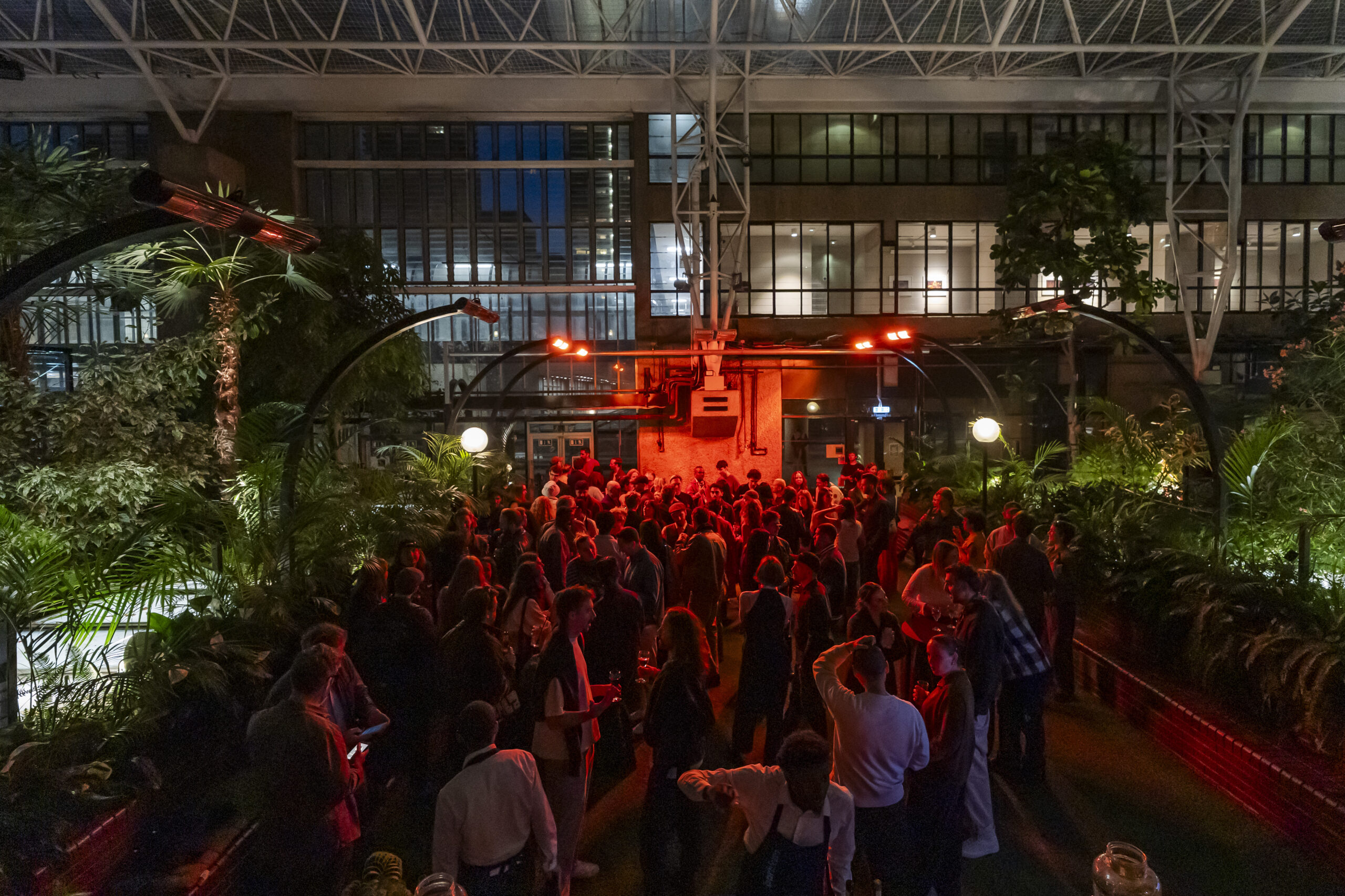 Crowd enjoying night event in greenhouse garden.