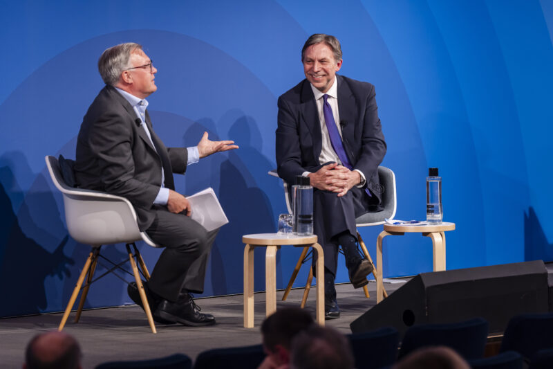 Two men in discussion on stage with blue background.