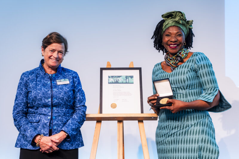 Two women with award certificate and medal on stage.